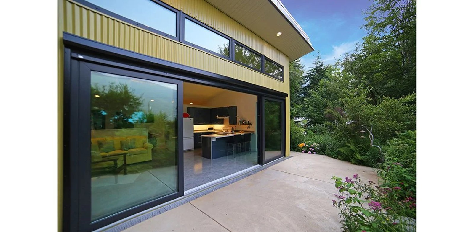 Exterior view of a wide sliding glass door open into the kitchen beneath clerestory windows